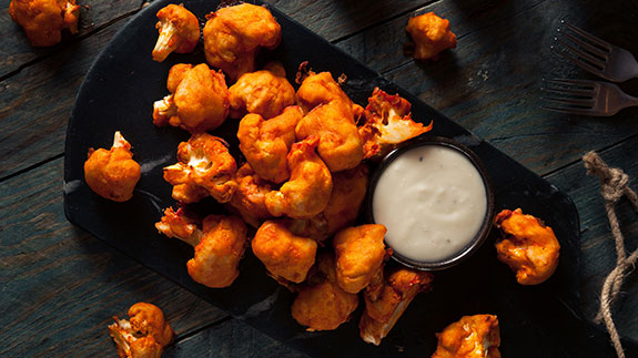 Buffalo Cauliflower Bites made with Frank’s RedHot Sauce served on a black plate with a creamy dipping sauce